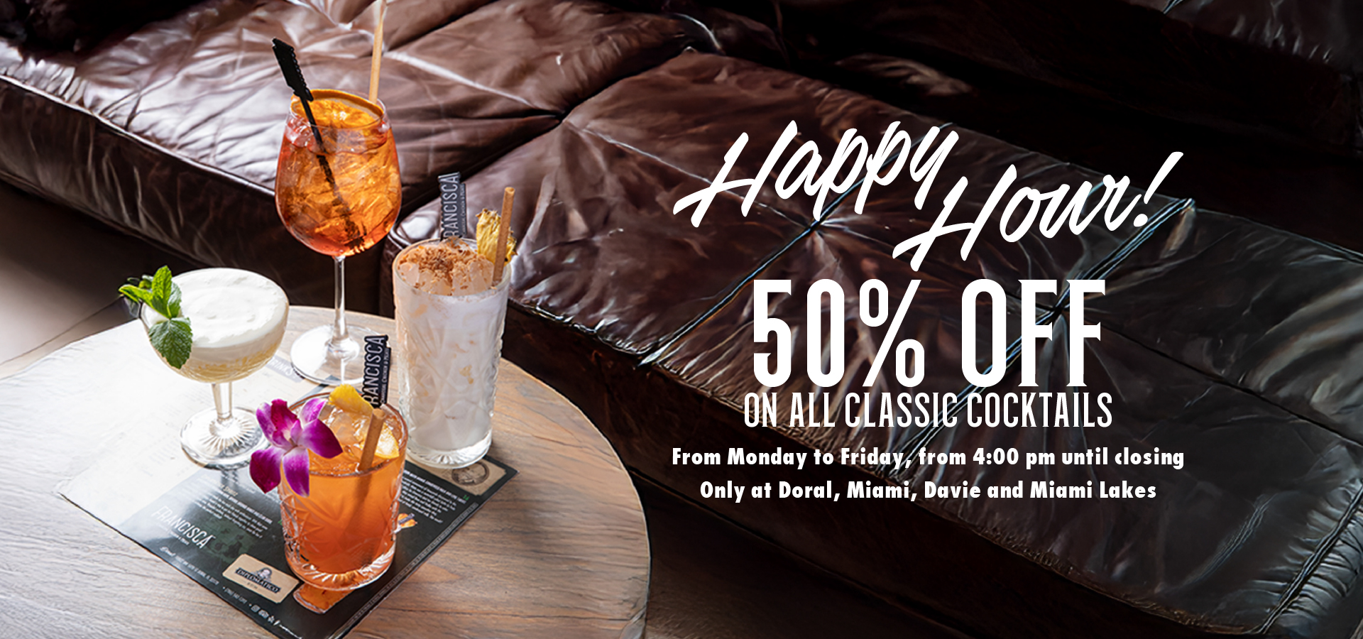 Four colorful cocktails sit on a wooden table beside a dark leather couch. Text reads: “Happy Hour! 50% off on all classic cocktails. From Monday to Friday, from 4:00 pm until closing. Only at Doral, Miami, Davie and Miami Lakes.”