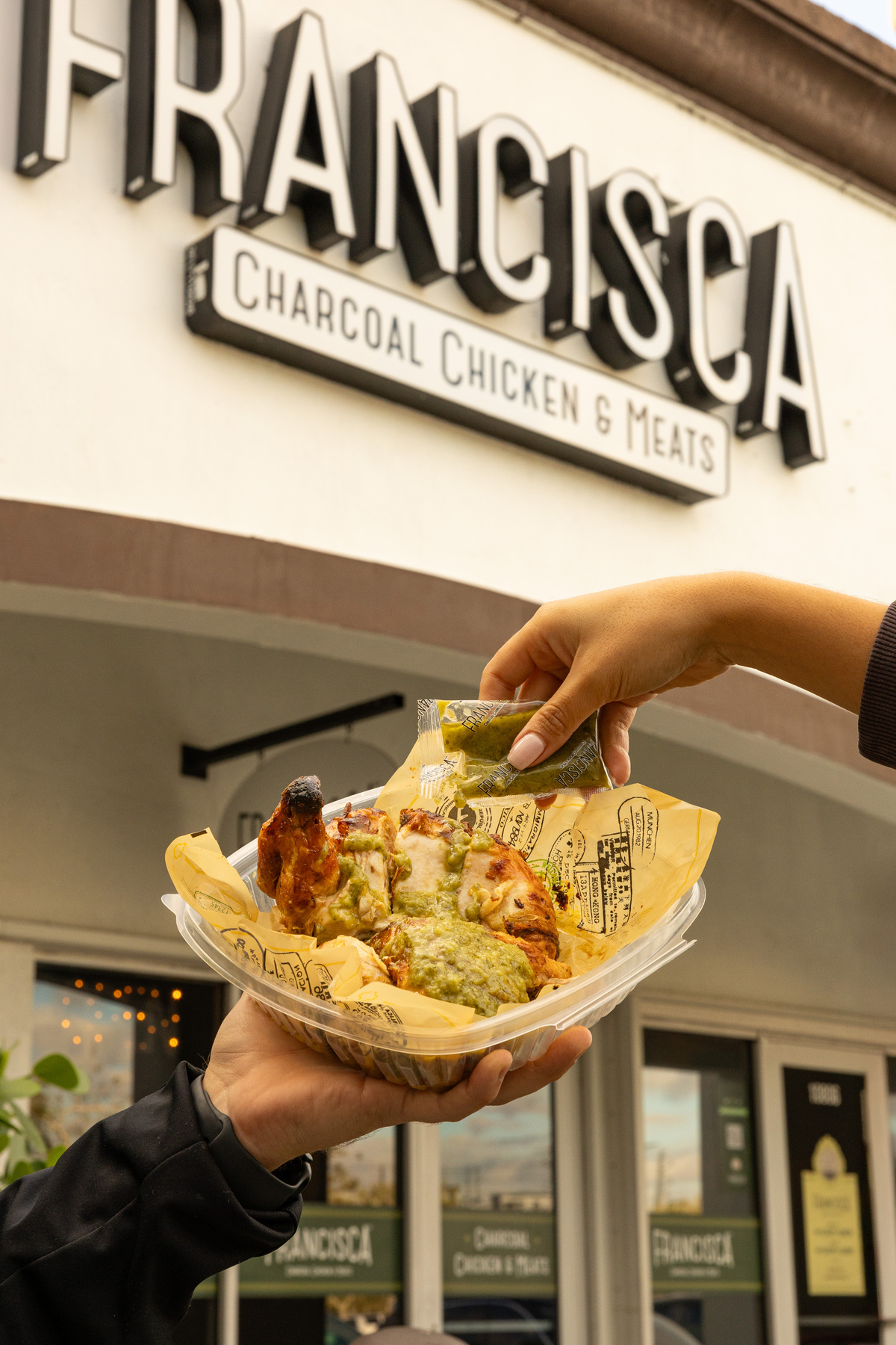 Image of a person holding a container with chicken, pouring sauce on it.
