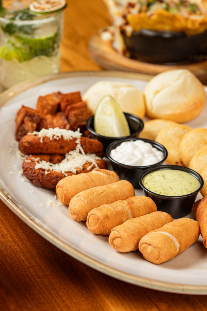 Close-up photo of a plate with tequeños, food, and sauce.