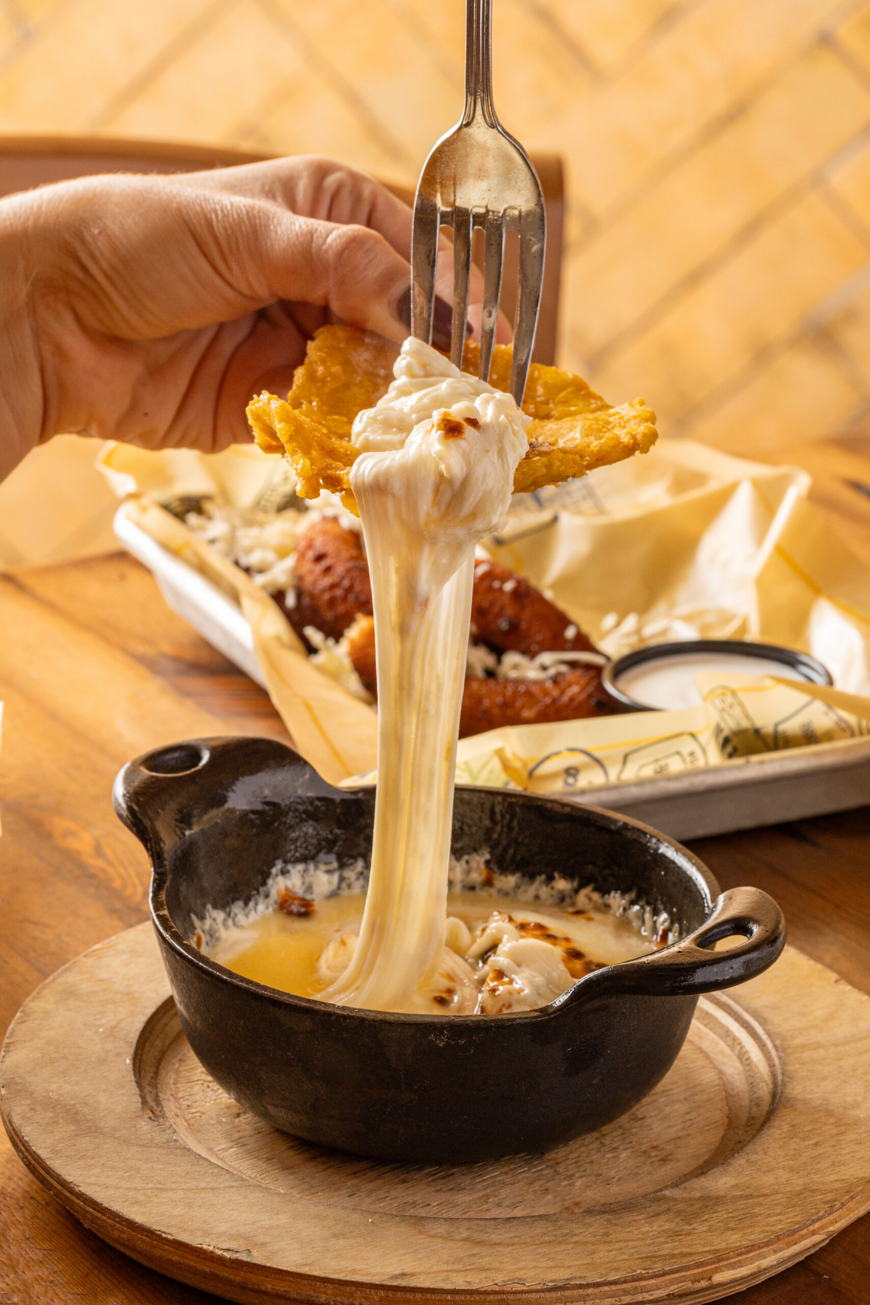 A close-up image of a person holding a piece of food and pouring cheese over it.