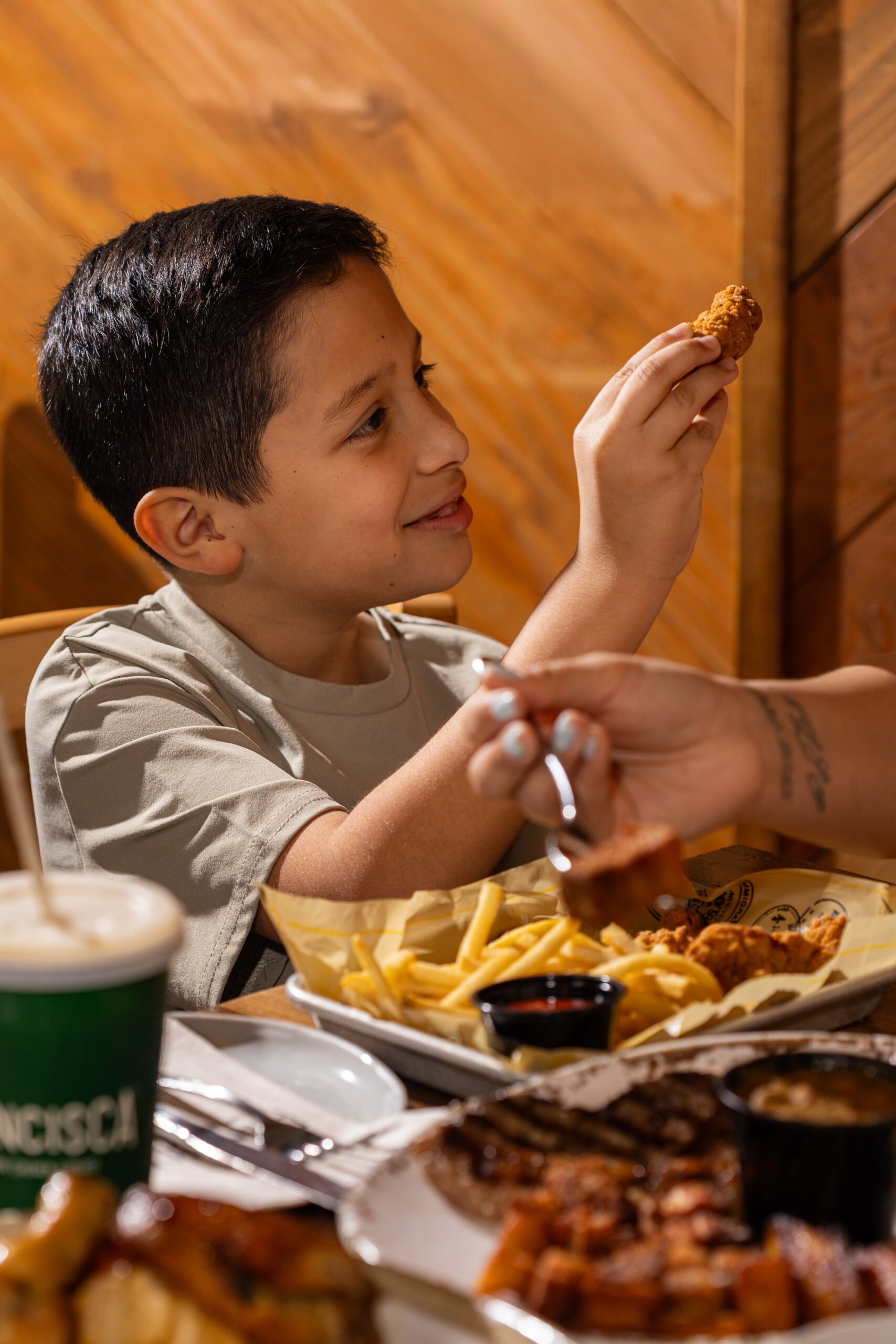 Child holding a chicken bite at a table with fries and dipping sauces.