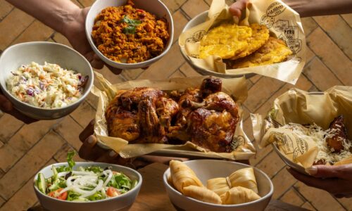 Overhead view of a Cuban-style meal featuring roasted chicken, rice, tostones, tamales, coleslaw, salad, and fried plantains served in bowls